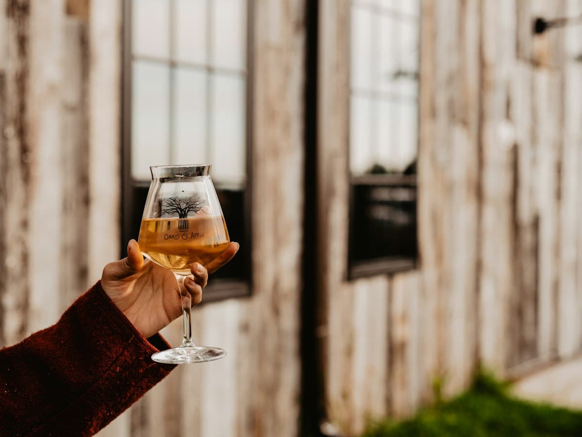 A glass of hard cider raised outside a barn